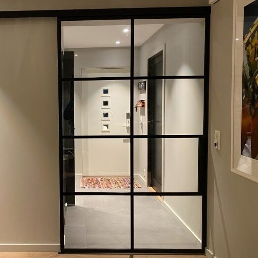 Utenpåliggende-enkel-skyvedør-i-metall-med-glass-installert-i-minimalistisk-interiør