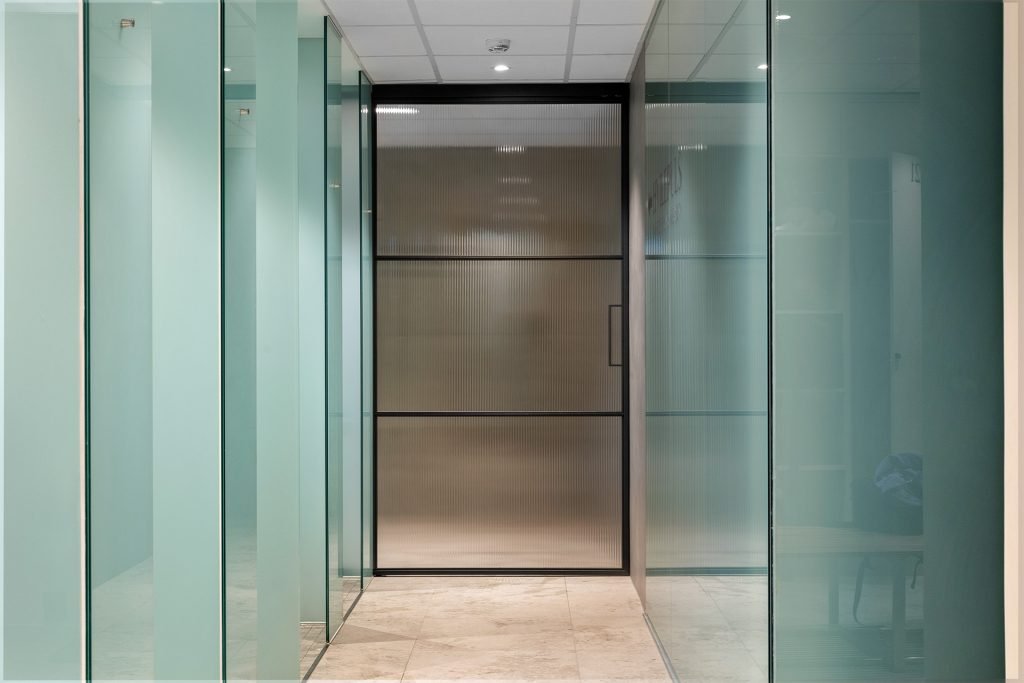 Utenpåliggende skyvedør i metall og glass med rillet glass i gang